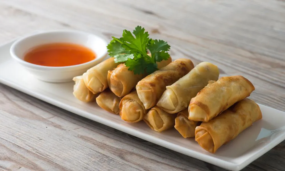 Crispy golden fried spring rolls stacked on white rectangular plate with sweet chili dipping sauce and cilantro garnish at Princess Dumpling, a Asian Restaurant in Rowland Heights