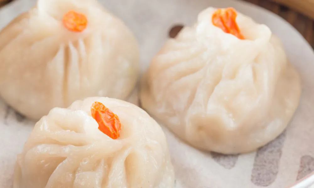 Steaming bamboo steamer filled with eight pleated white xiao long bao soup dumplings over wooden table surface at Princess Dumpling, a Asian Restaurant in Rowland Heights