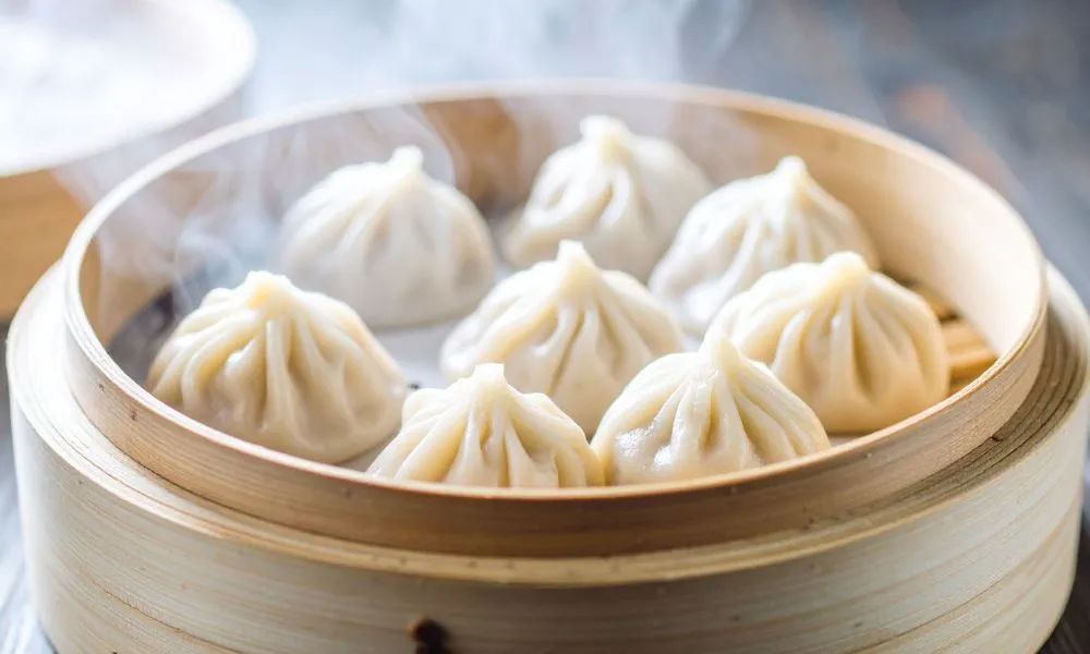 Steaming bamboo steamer filled with eight pleated white xiao long bao soup dumplings over wooden table surface at Princess Dumpling, a Asian Restaurant in Rowland Heights