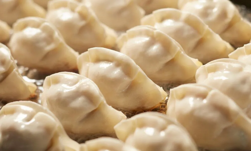 Close-up shot of glossy uncooked pan-fried dumplings resting in hot oil on metal cooking tray at Princess Dumpling, a Asian Restaurant in Rowland Heights