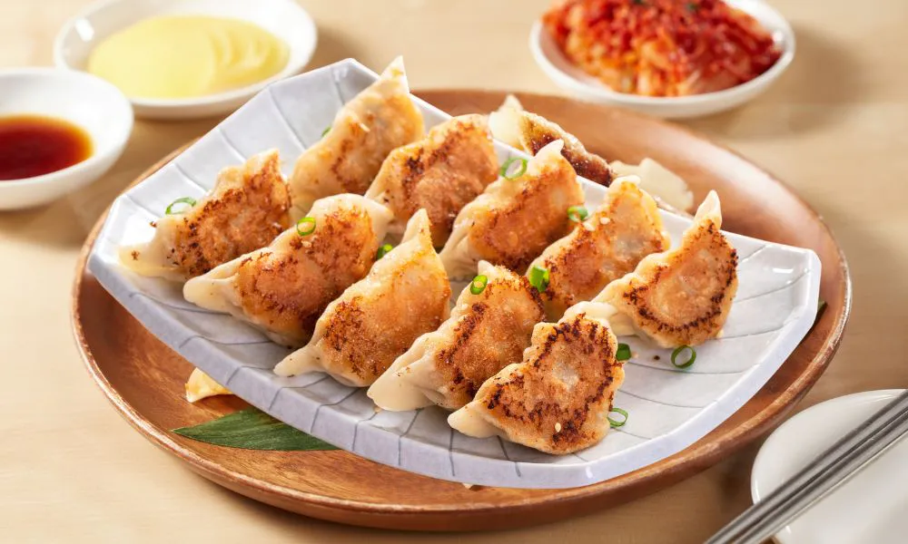 Plate of golden crispy pan-fried dumplings garnished with green onions, soy sauce and kimchi side dishes at Princess Dumpling, a Asian Restaurant in Rowland Heights